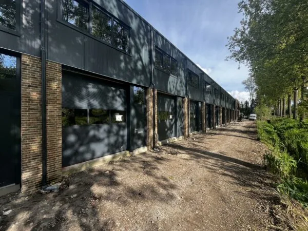 Rij moderne bedrijfsunits aan de Broekdijk West 19-4 met onverharde weg en bomenrij.